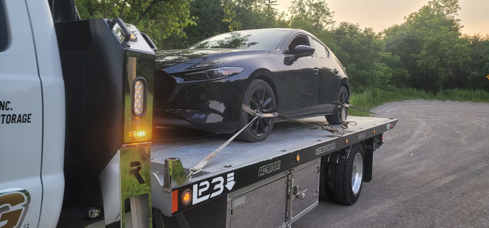 Black Mazda 3 hatchback secured on flatbed at sunset in Durham Region