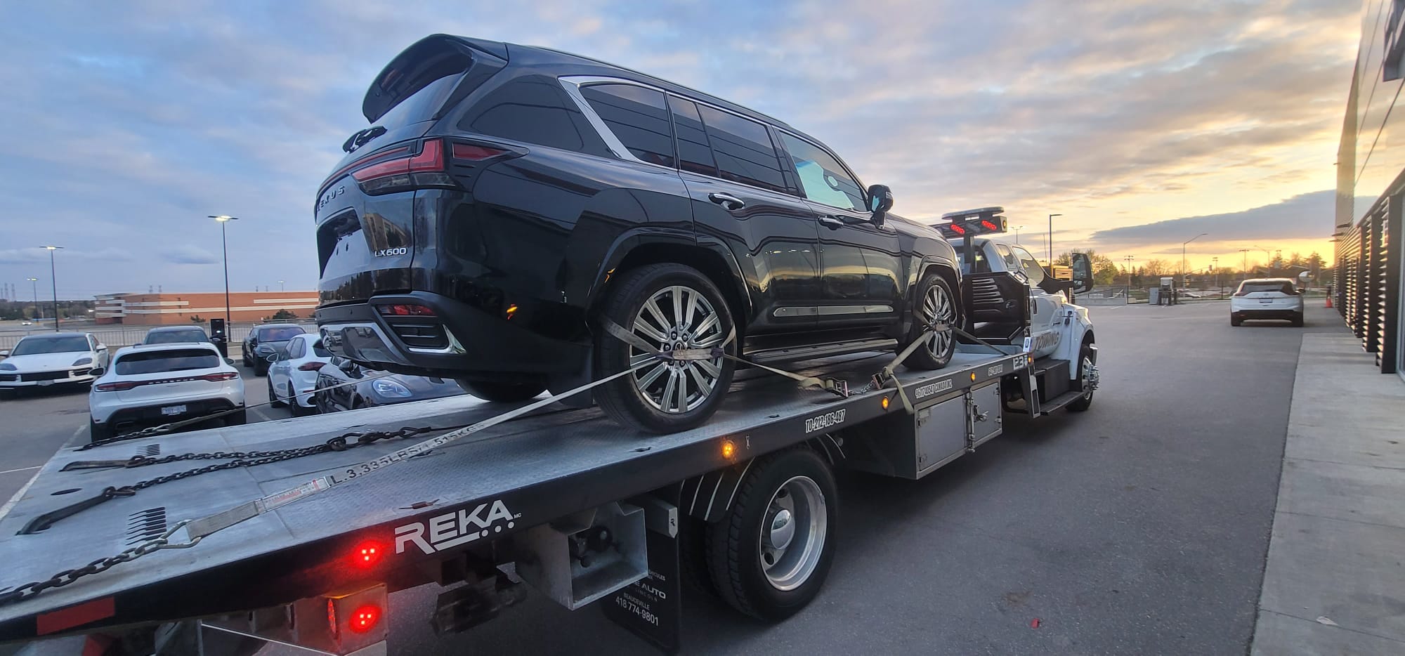 Black Lexus LX600 SUV secured on flatbed for delivery at sunset