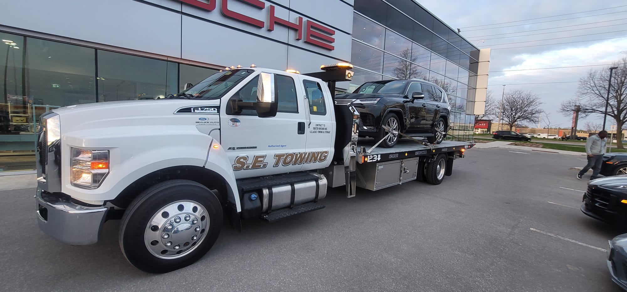 S.E. Towing F-750 flatbed delivering a black Lexus LX600 to a Porsche dealership