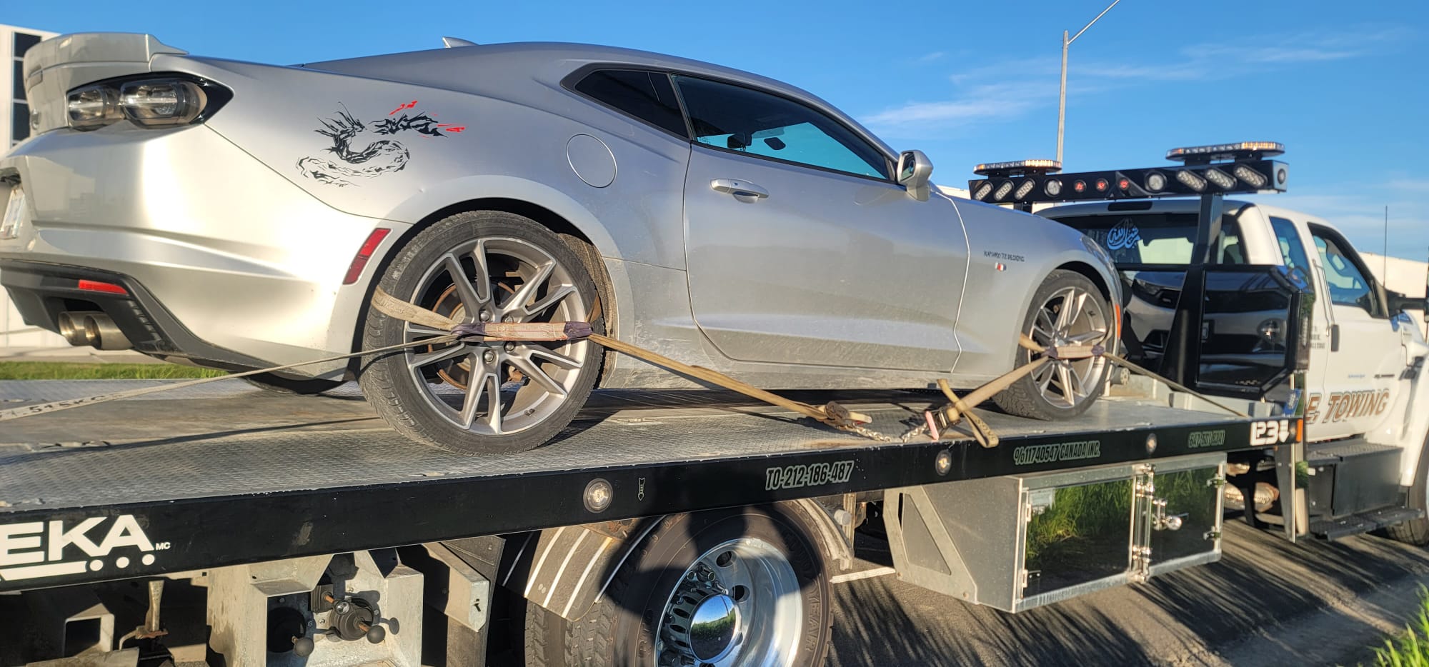 Silver Chevrolet Camaro sports car secured on flatbed at sunrise