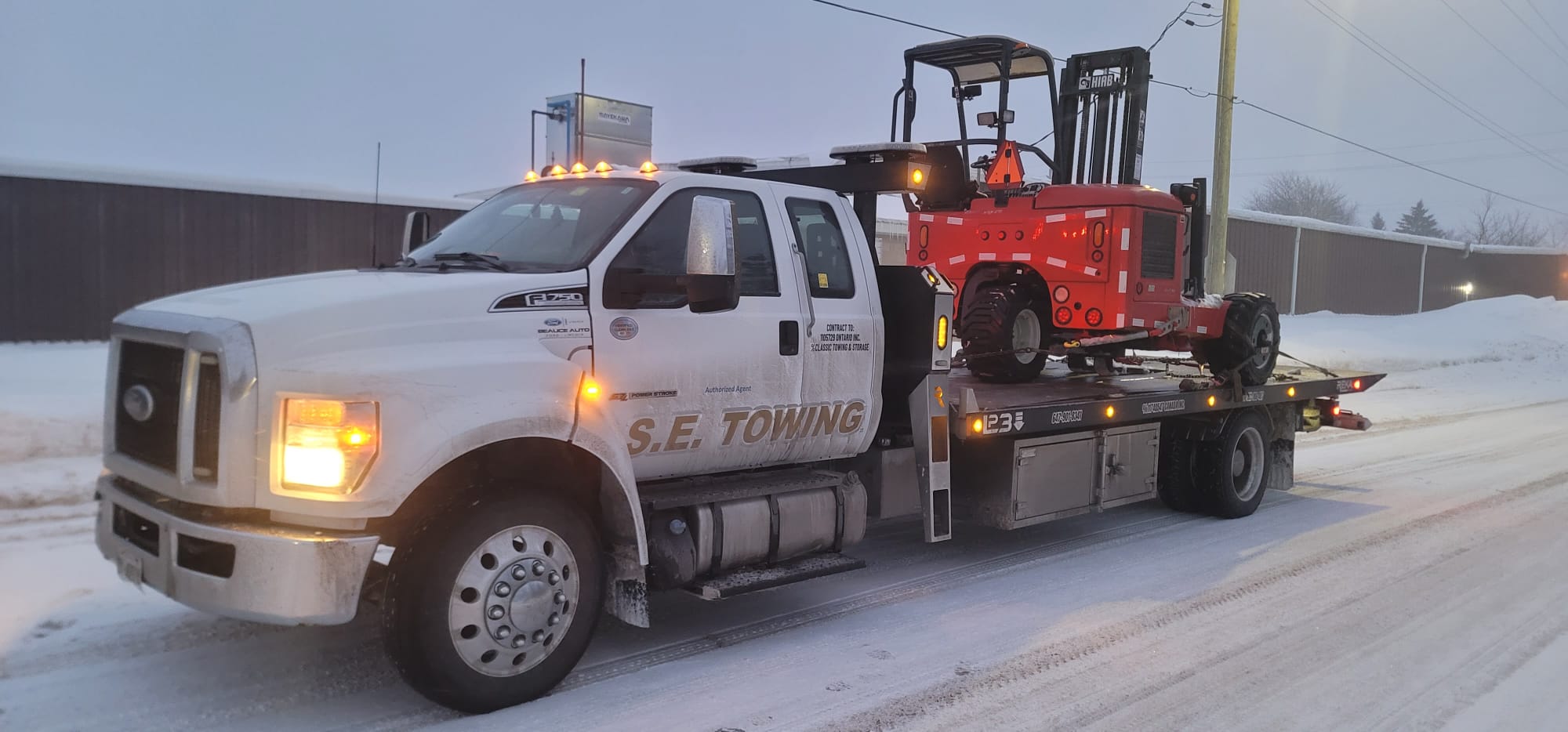 S.E. Towing F-750 flatbed transporting a red industrial forklift in winter