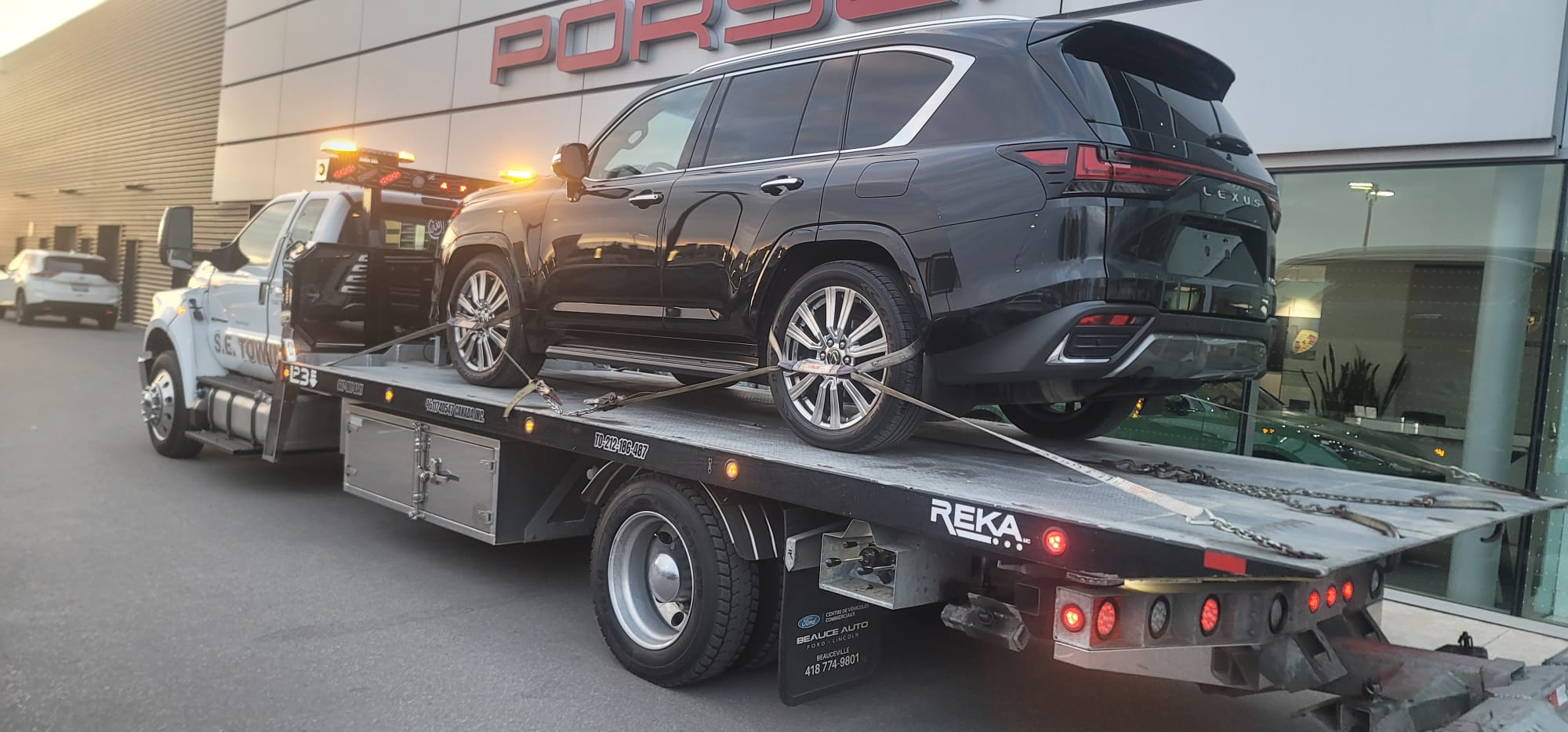 Black Lexus SUV being transported outside Porsche dealership by S.E. Towing