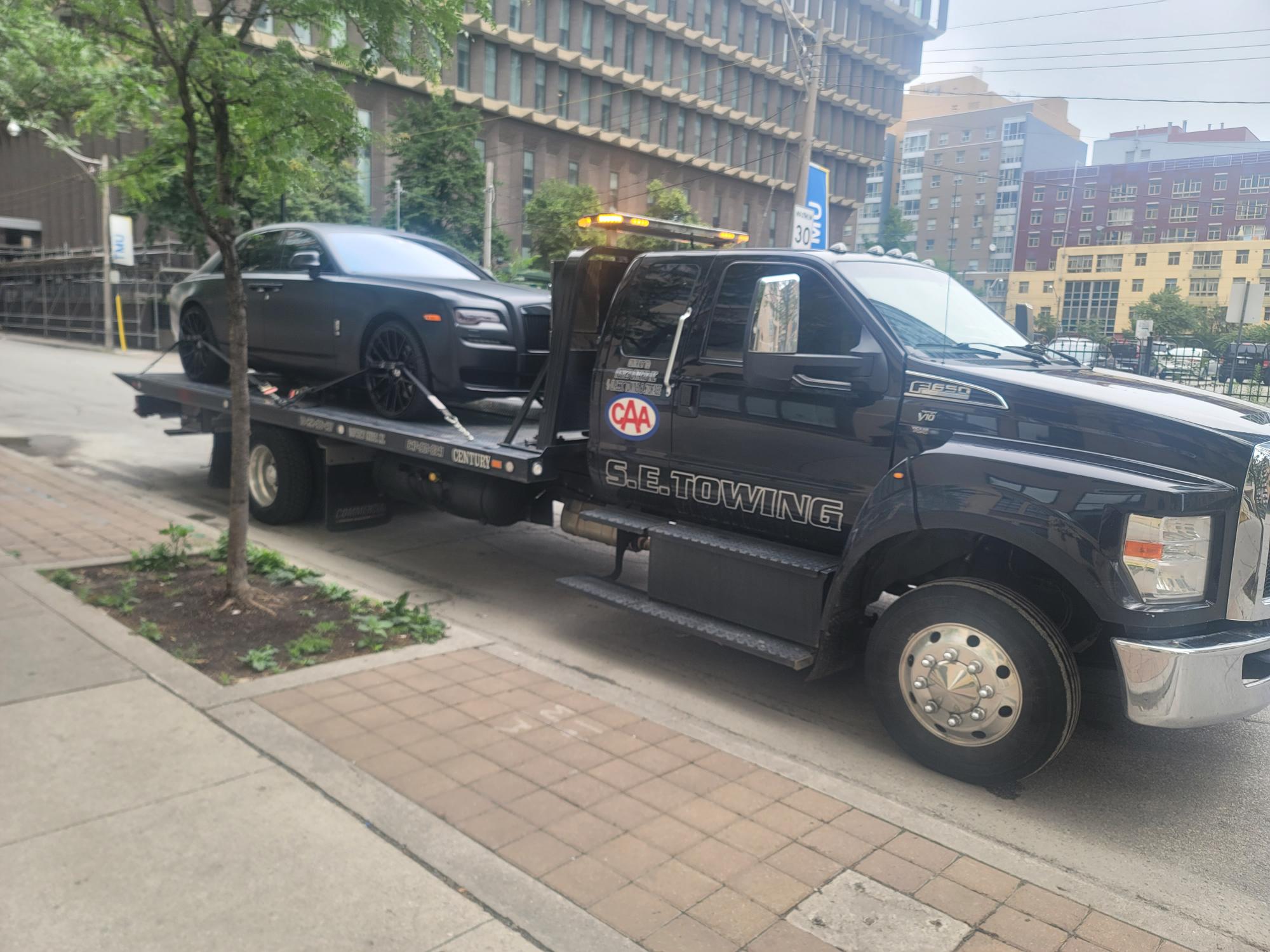 S.E. Towing flatbed with luxury sedan in downtown Toronto